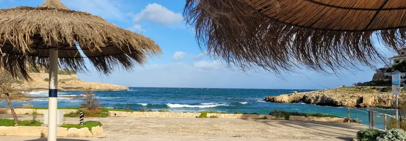 Blick unter Strohschirmen hindurch auf die Bucht der Cala Murada