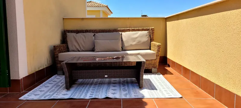 Sonnige Dachterrasse mit Rattan-Sofa und Outdoor-Teppich