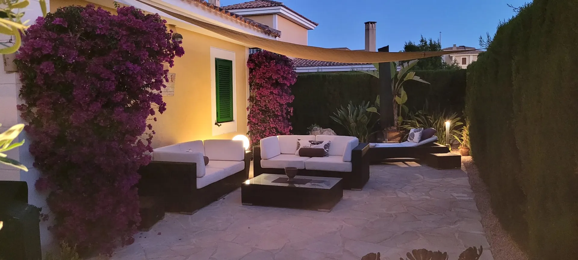 Lounge-Terrasse am Abend mit weißen Polstersofas und blühender Bougainvillea
