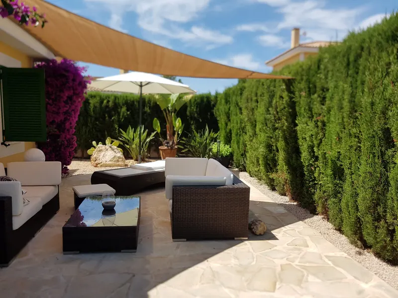 Terrasse mit Rattan-Loungemöbeln, Sonnensegel und Zypressenhecke