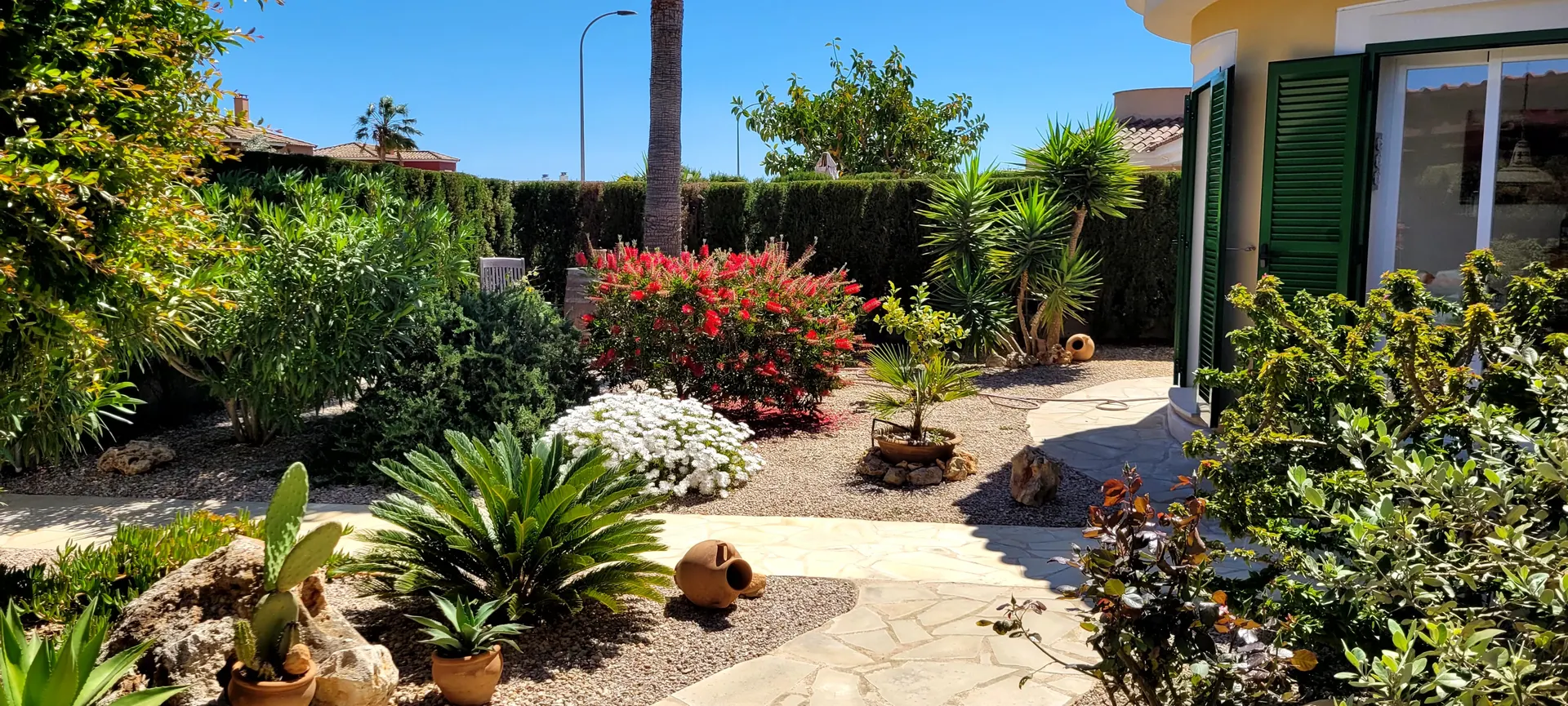 Die gelbe mallorquinische Villa Cala Murada mit grünen Fensterläden und üppig bepflanztem Vorgarten